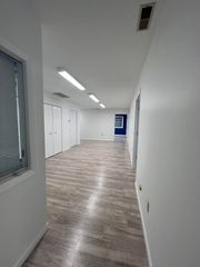 Empty office hallway with white walls, wood-look flooring, and doors along the left side.