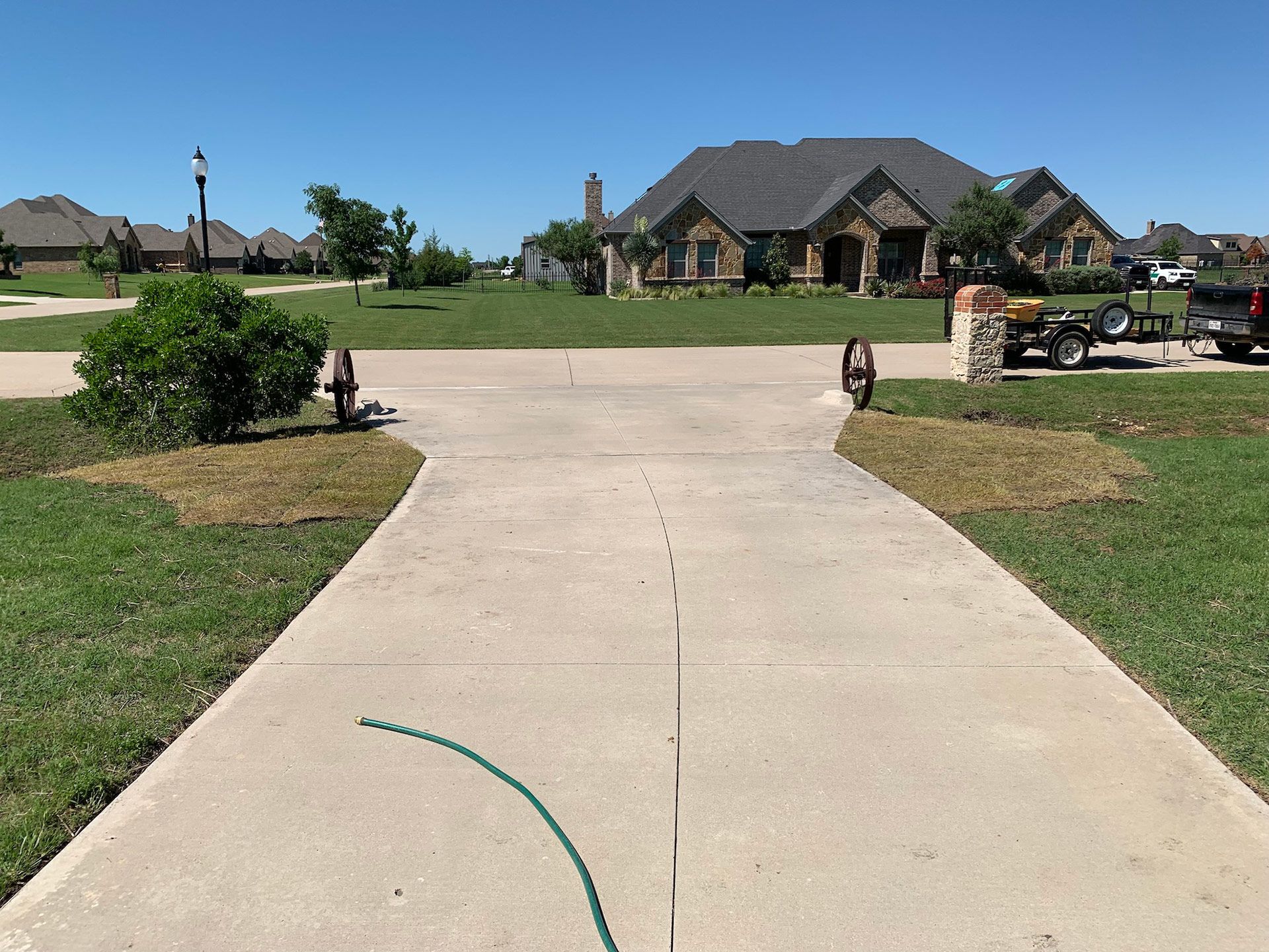 Wide concrete driveway leading to a two-story house with a green lawn on a sunny day.