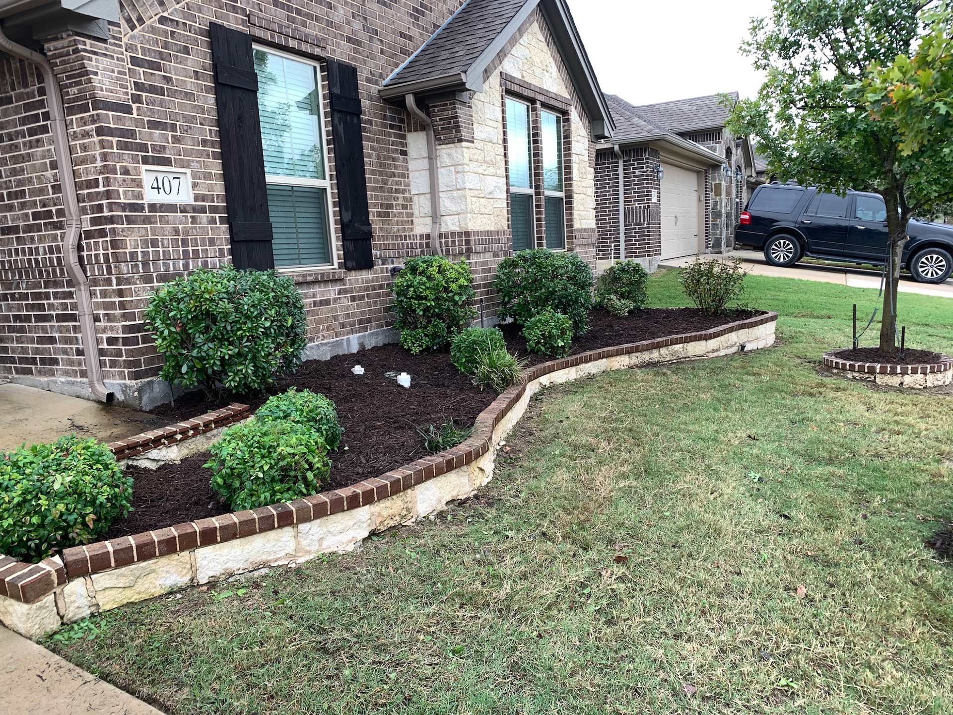 Brick house with landscaping, bushes in a mulch-filled bed, and a car in the driveway.