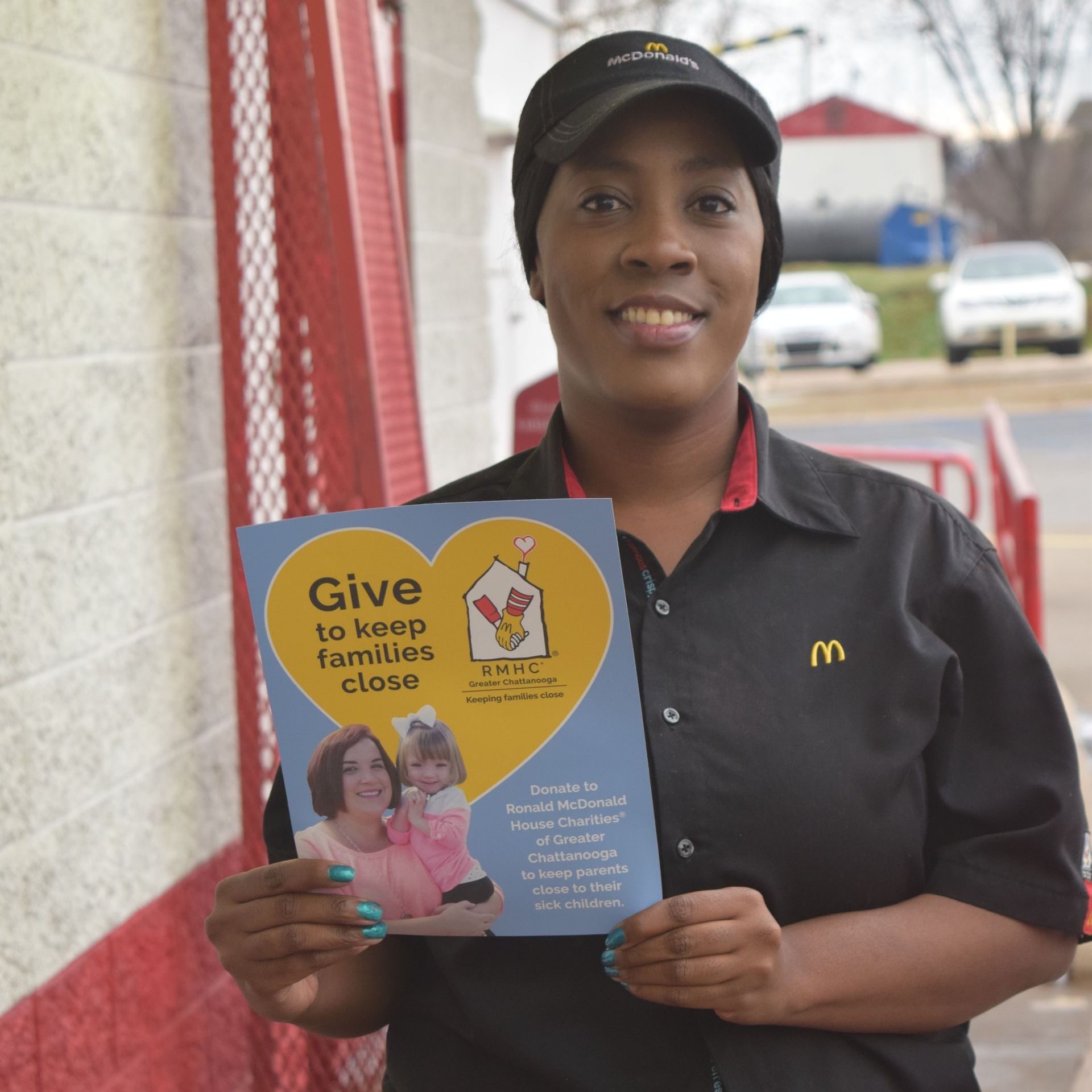 A woman in a mcdonald 's uniform is holding a pamphlet that says give to keep families close