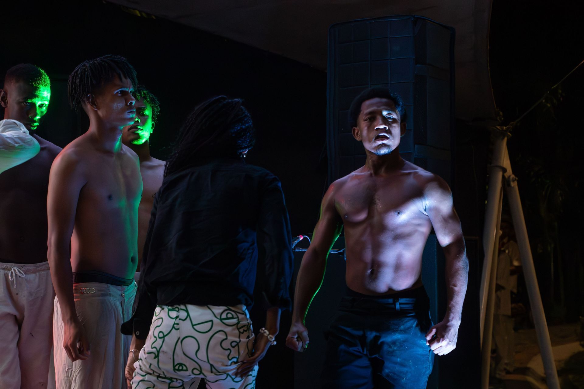 Un grupo de hombres sin camisa están parados uno al lado del otro en una habitación oscura. | Memorias danza teatro