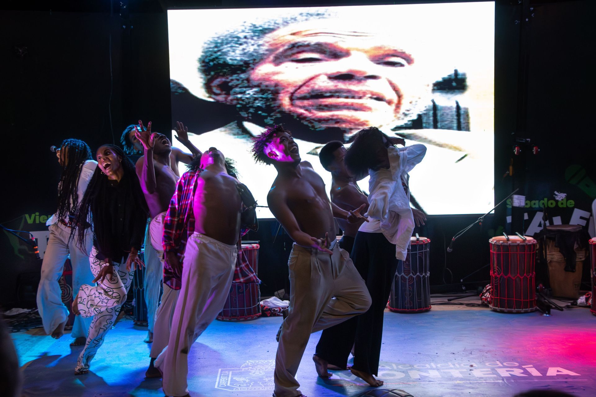 Un grupo de personas está bailando en un escenario frente a una pantalla grande. | Memorias danza teatro