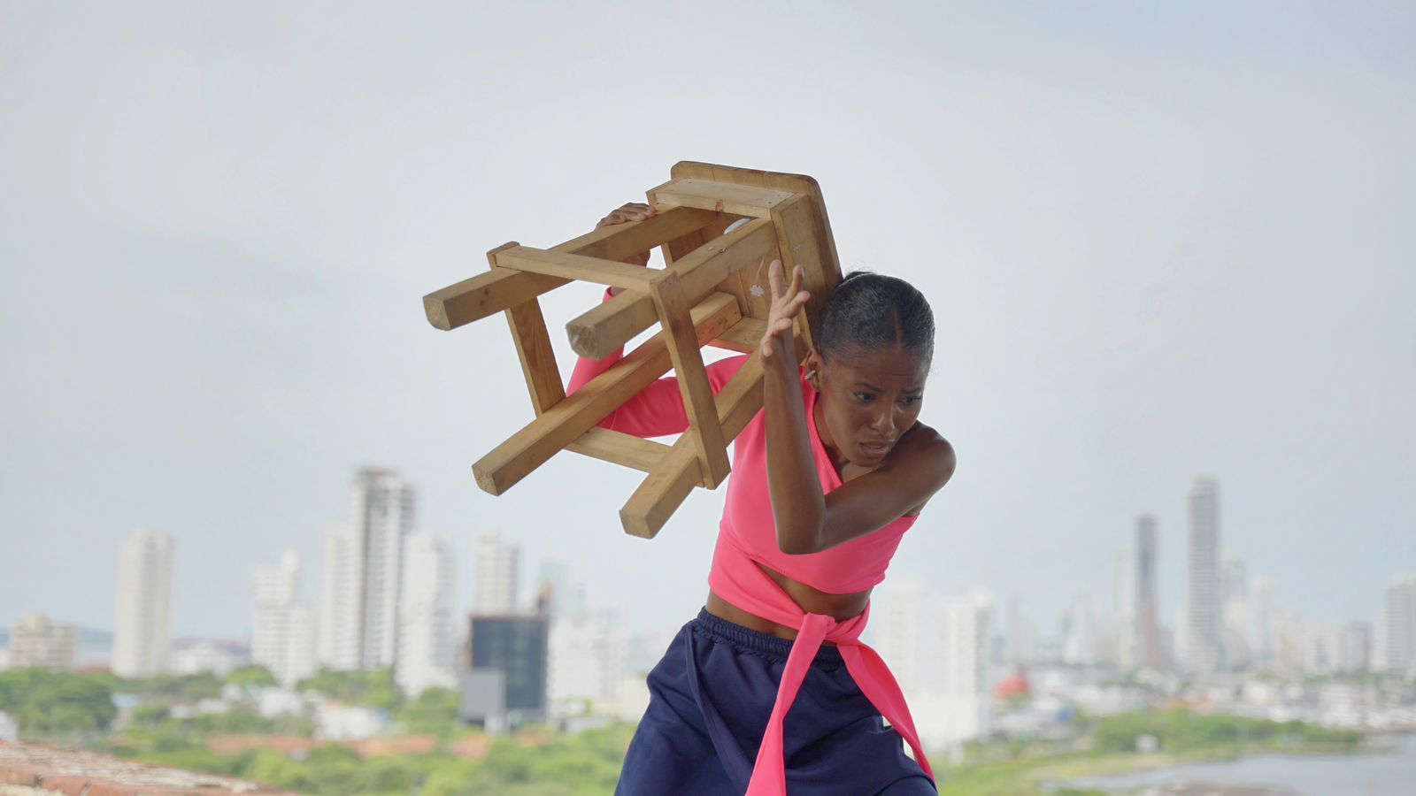 Una niña lleva una silla de madera en su espalda.