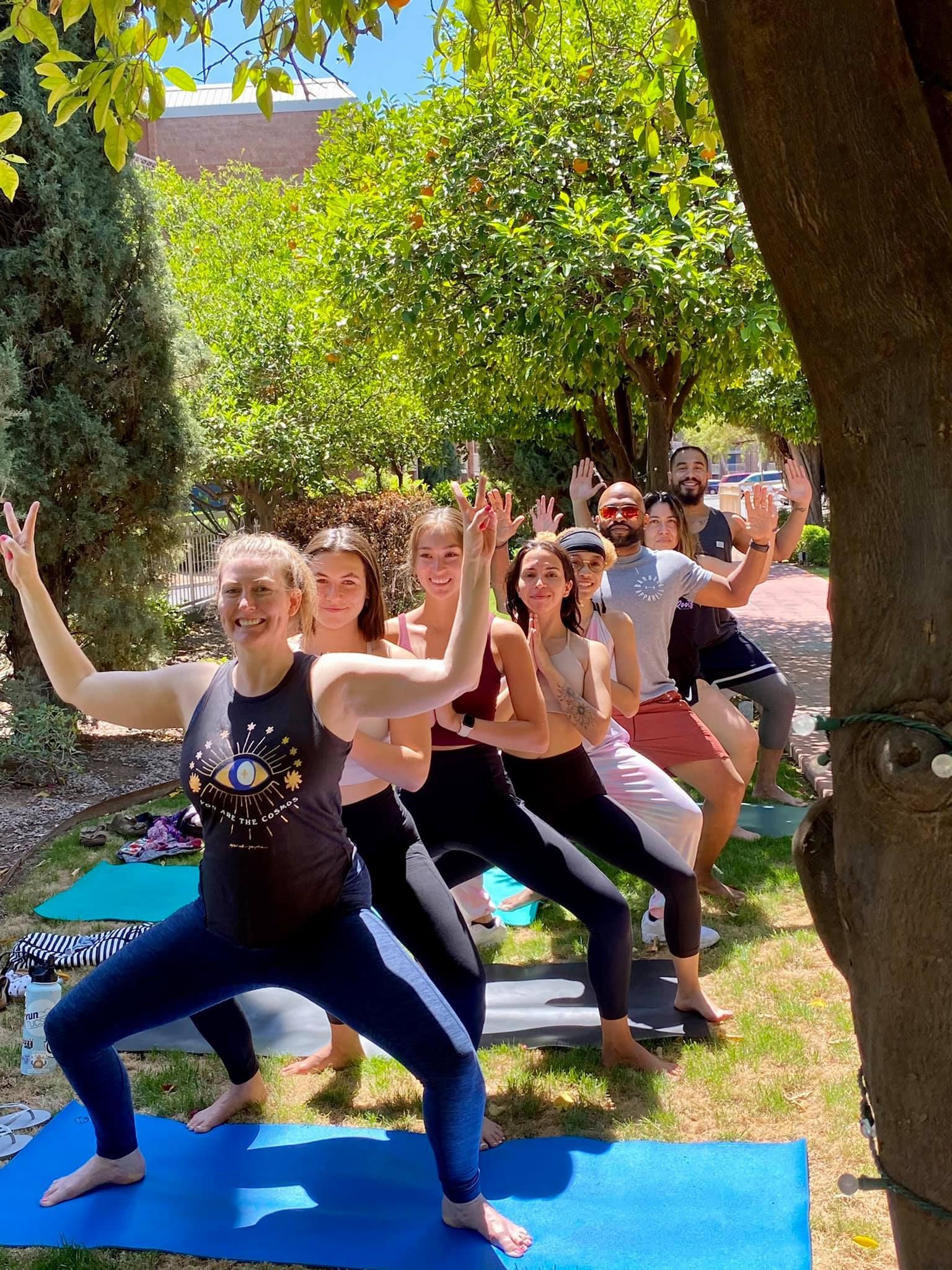 Group of people doing yoga outside, arms raised in a
