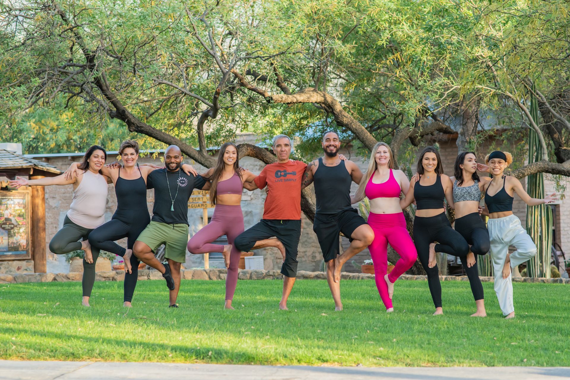 Group of people in tree pose on grass, trees in background.