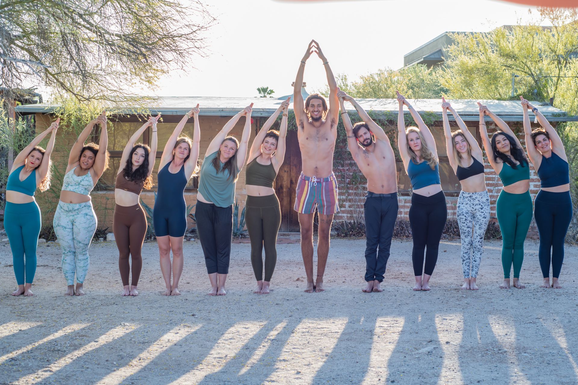 Group of people in yoga poses outdoors with arms overhead.