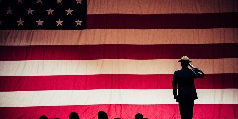 military service member saluting in front of a large American flag during a patriotic ceremony