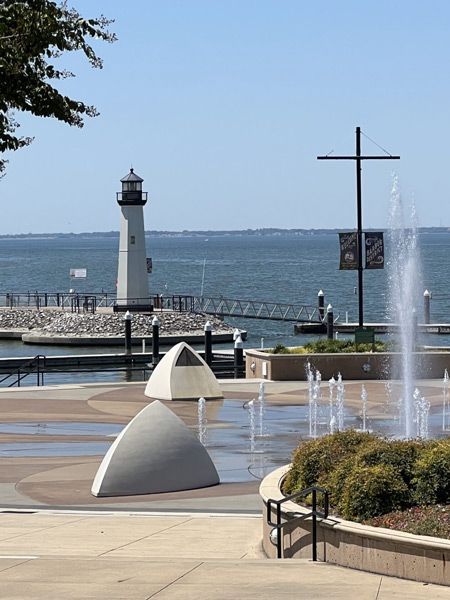 Lighthouse and fountain on a seaside promenade with blue water and clear sky