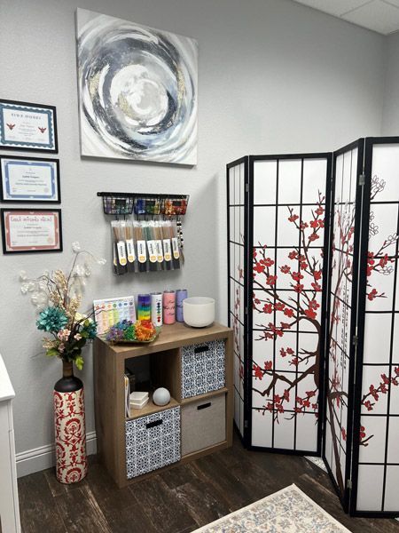 Small office corner with certificates, a water dispenser, shelf, and folding screen with red floral design.