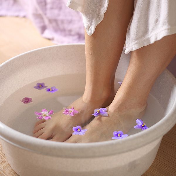 Feet soaking in a white basin of water with floating purple flowers