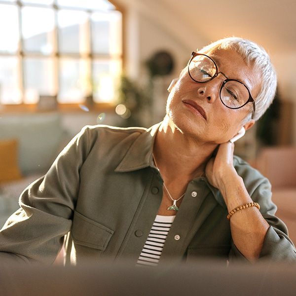 Person in glasses rests their head on one hand in a softly lit room, appearing tired or contemplative.