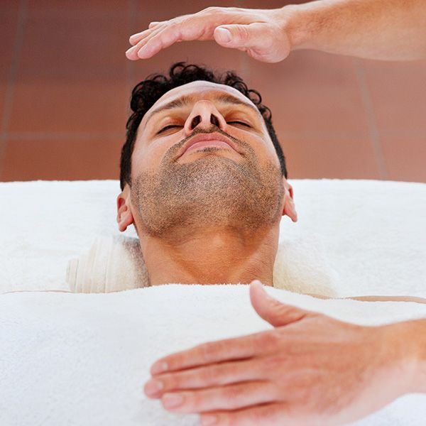 Person receiving a facial treatment with hands hovering over the face in a spa setting