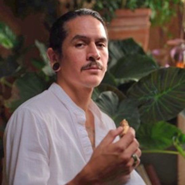 Person in a white shirt holding a small object, standing among lush green plants indoors.