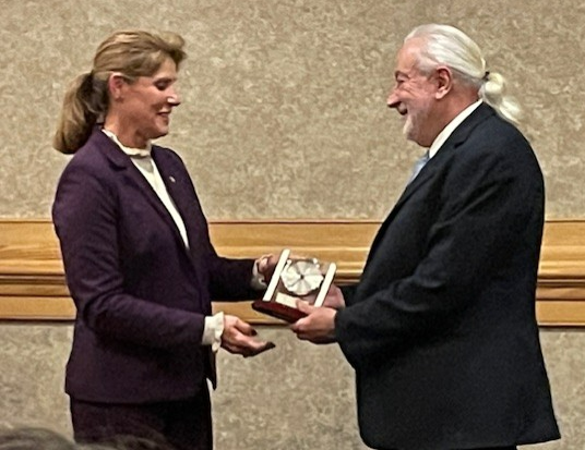 A man in a suit is giving a plaque to a woman in a purple suit— Akron, OH — Summit Psychological Associates, Inc