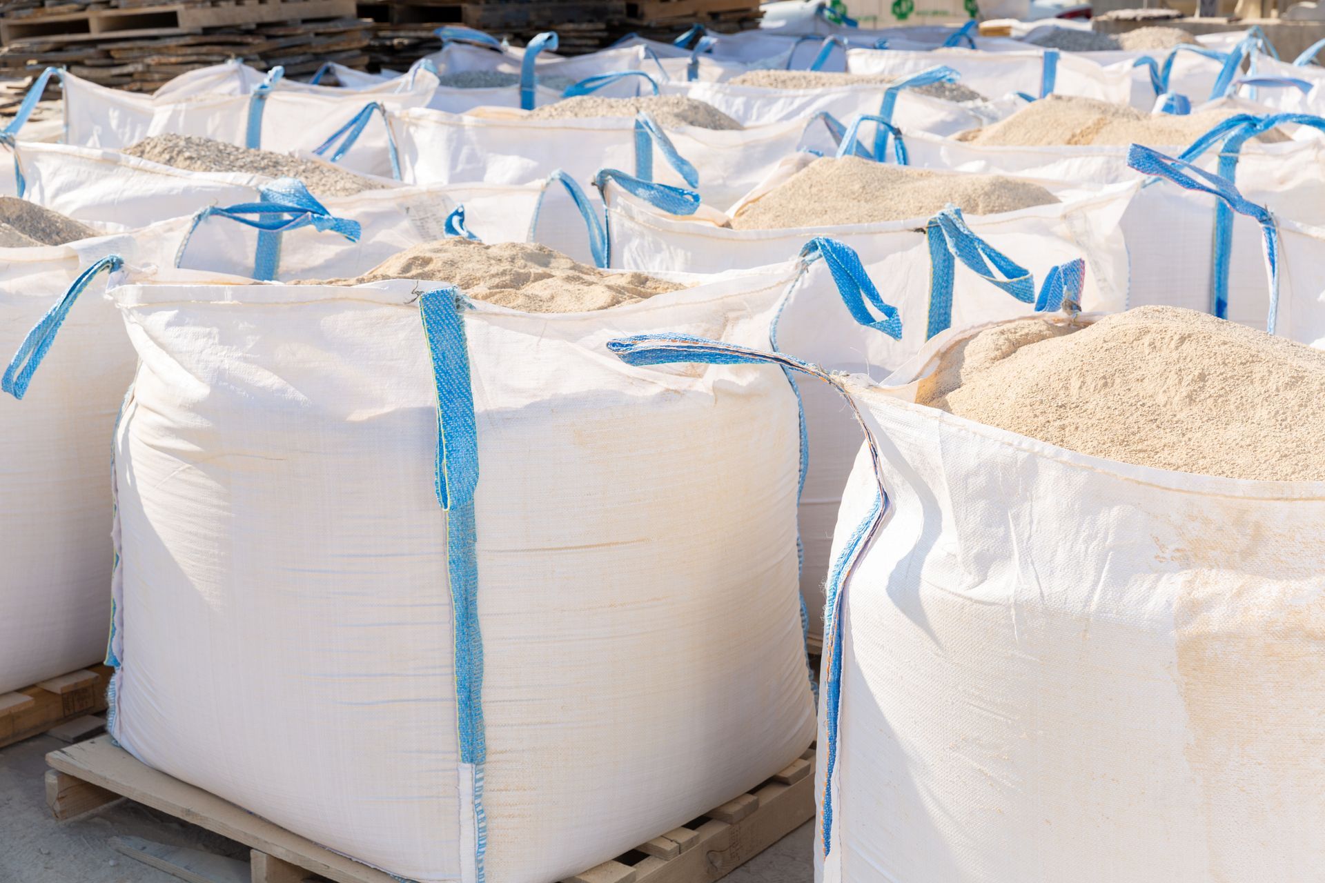 Bags filled with bulk construction materials stand in rows in outdoor storage. Bags filled with bulk construction materials stand in rows in outdoor storage.