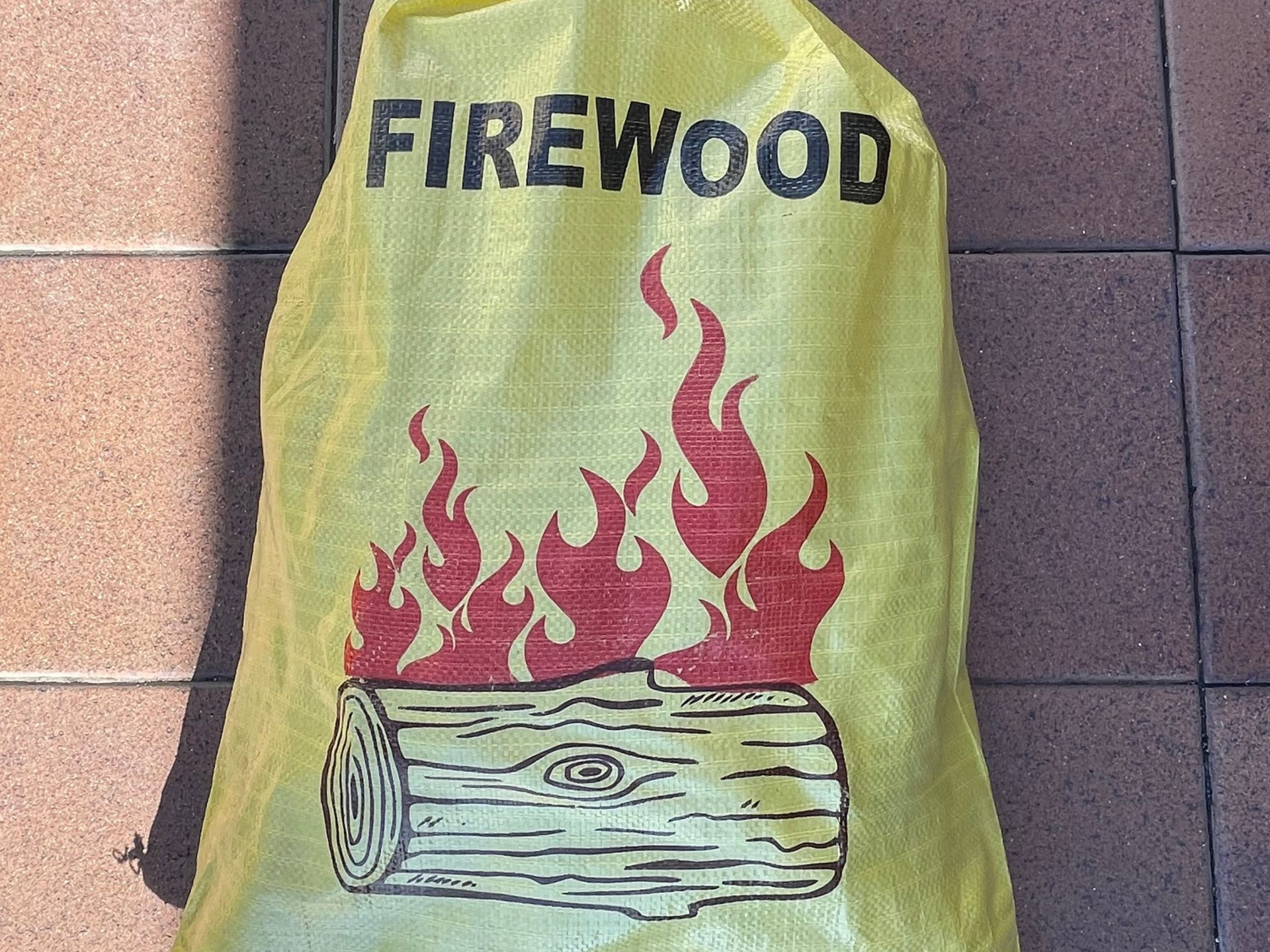 Yellow firewood bag with flame graphic on a tiled floor