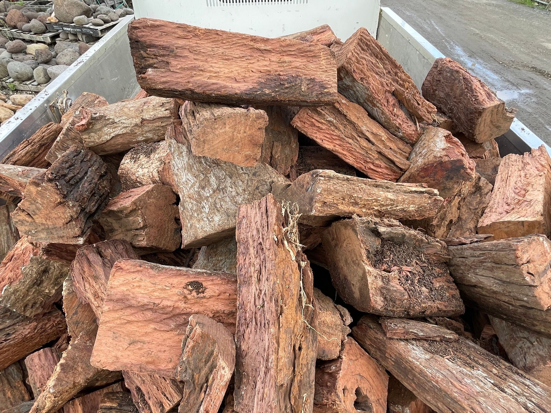 Pile of rough-cut red and tan wood planks stacked in a trailer outdoors