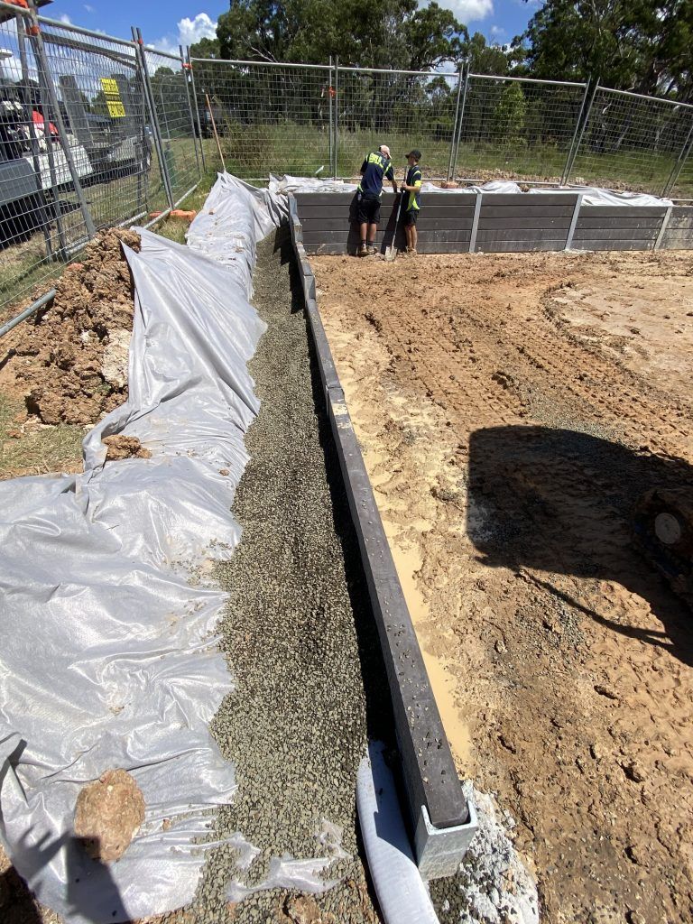 Construction site trench lined with white plastic, gravel channel, and workers in the background Construction site trench lined with white plastic, gravel channel, and workers in the background