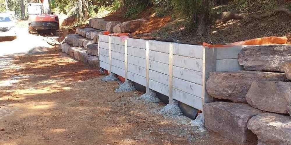 Wooden retaining wall along a dirt driveway beside stacked stone, with a car parked ahead