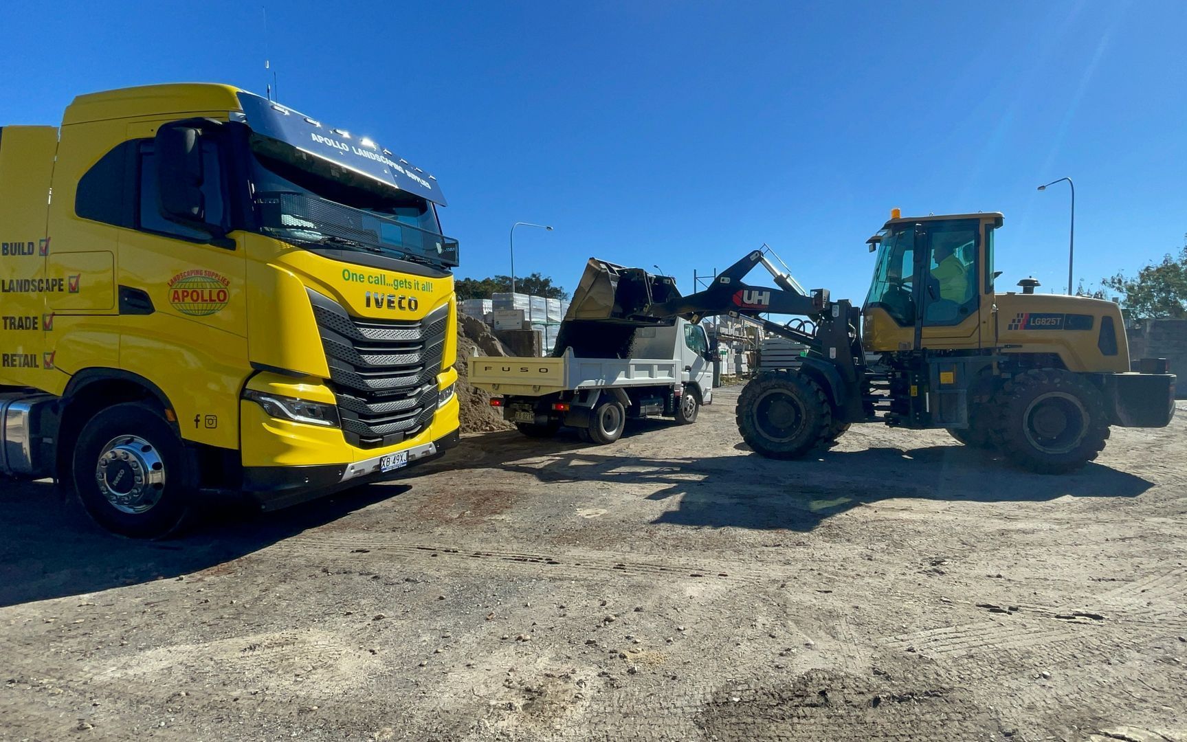 Yellow truck and wheel loader working on construction site, blue sky.