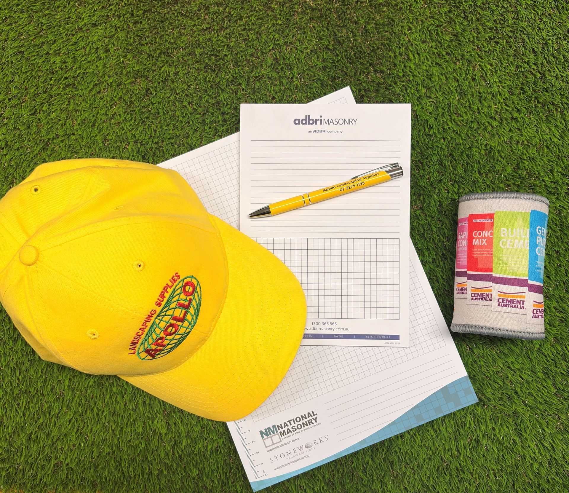 Yellow cap and notepad with a pen next to a can on green grass.