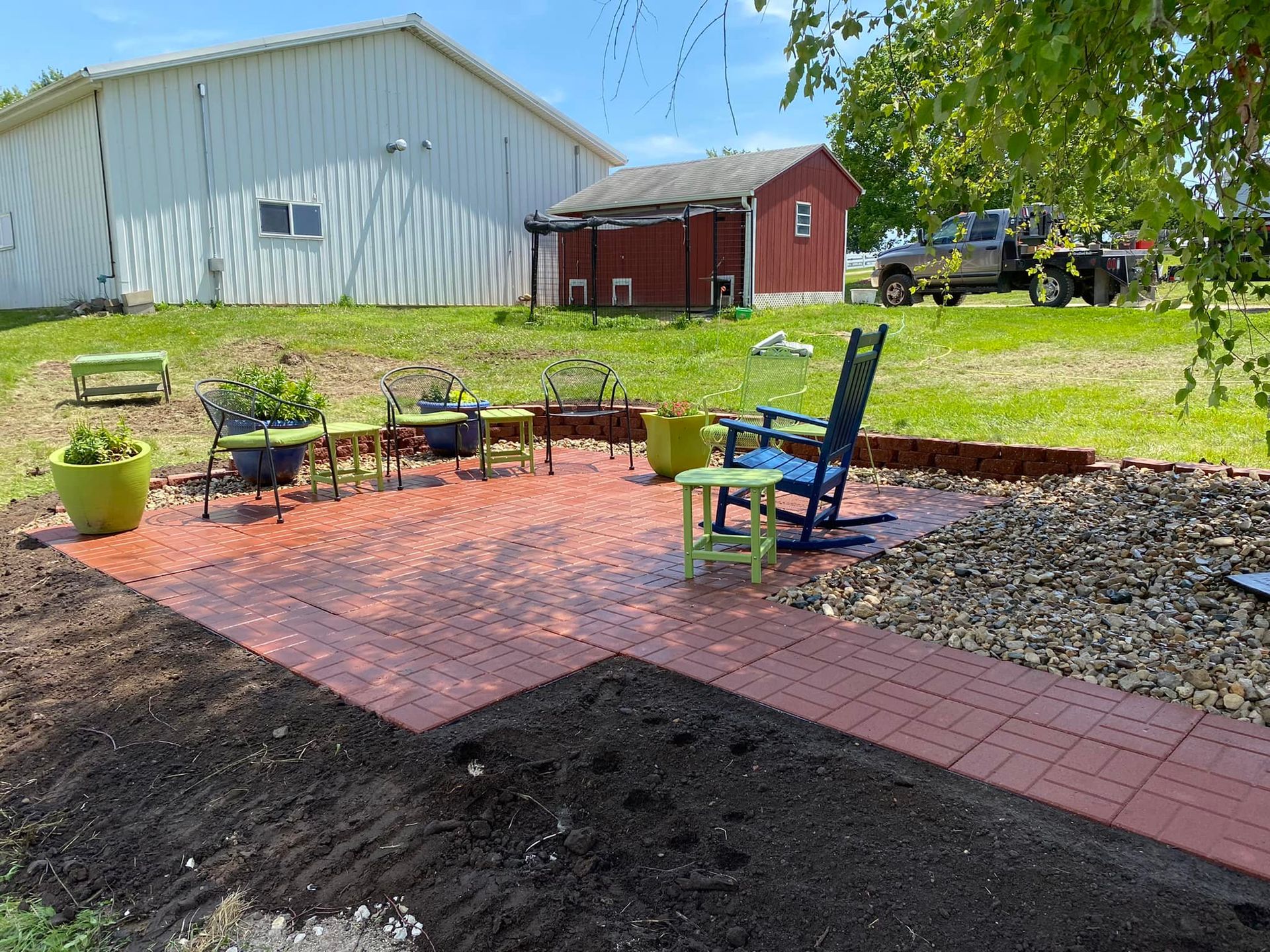 A rocking chair is sitting on a brick patio in front of a red barn.