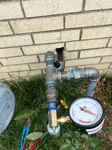 A water pressure gauge and plumbing against a brick wall.