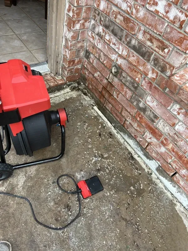 Red blower on concrete next to brick wall, with a control box and a doorway visible.