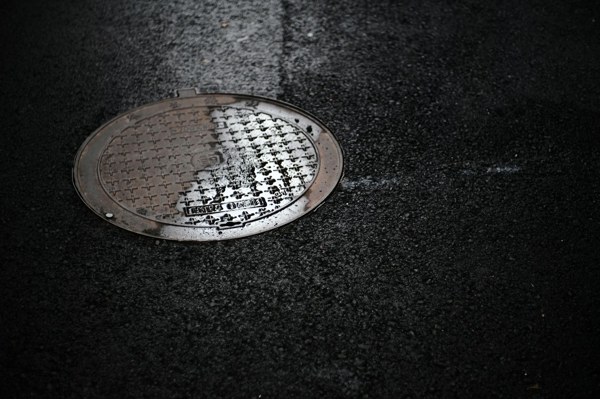 Round metal manhole cover on dark asphalt pavement