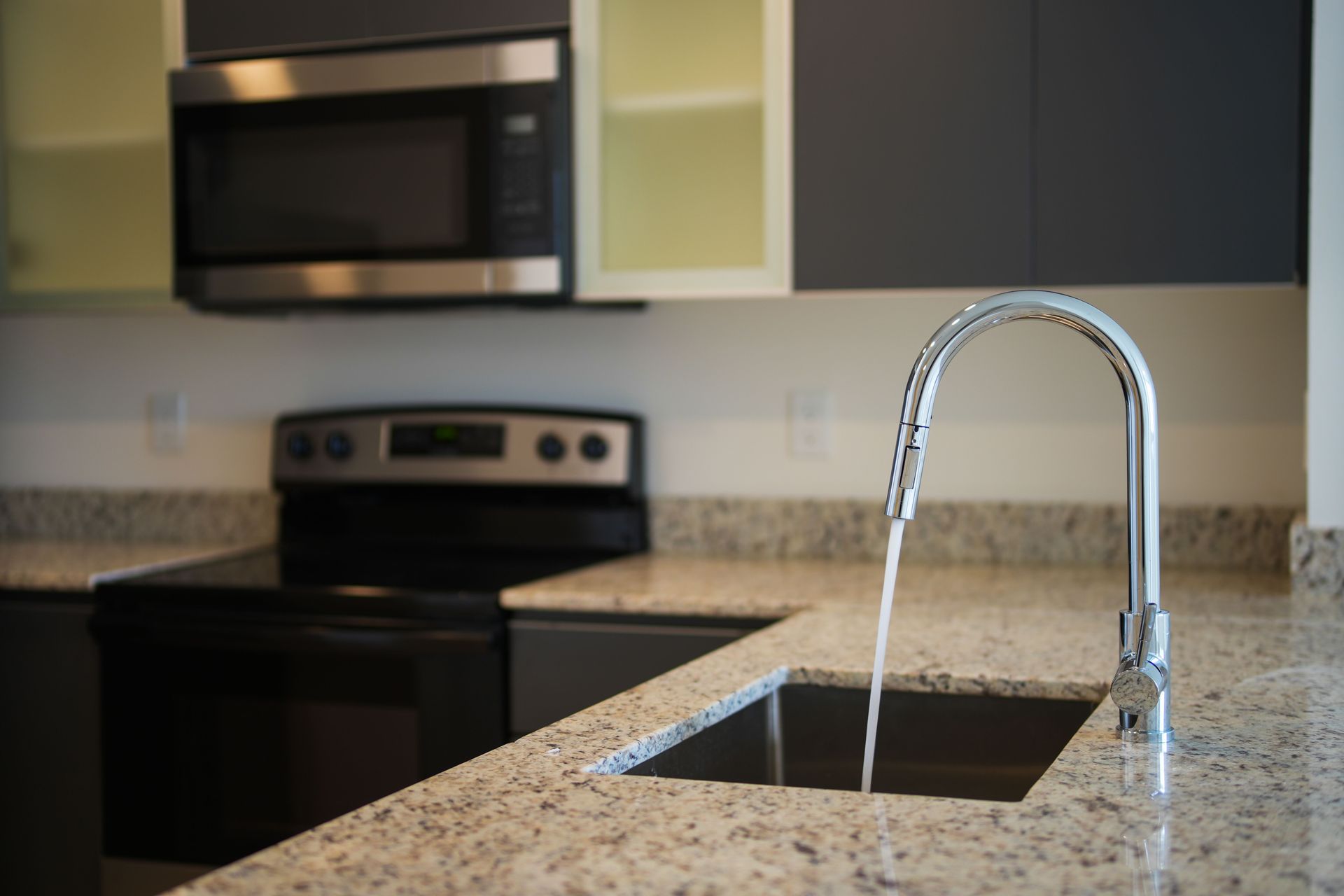 Modern kitchen with granite island and running faucet over sink, black stove and microwave in background