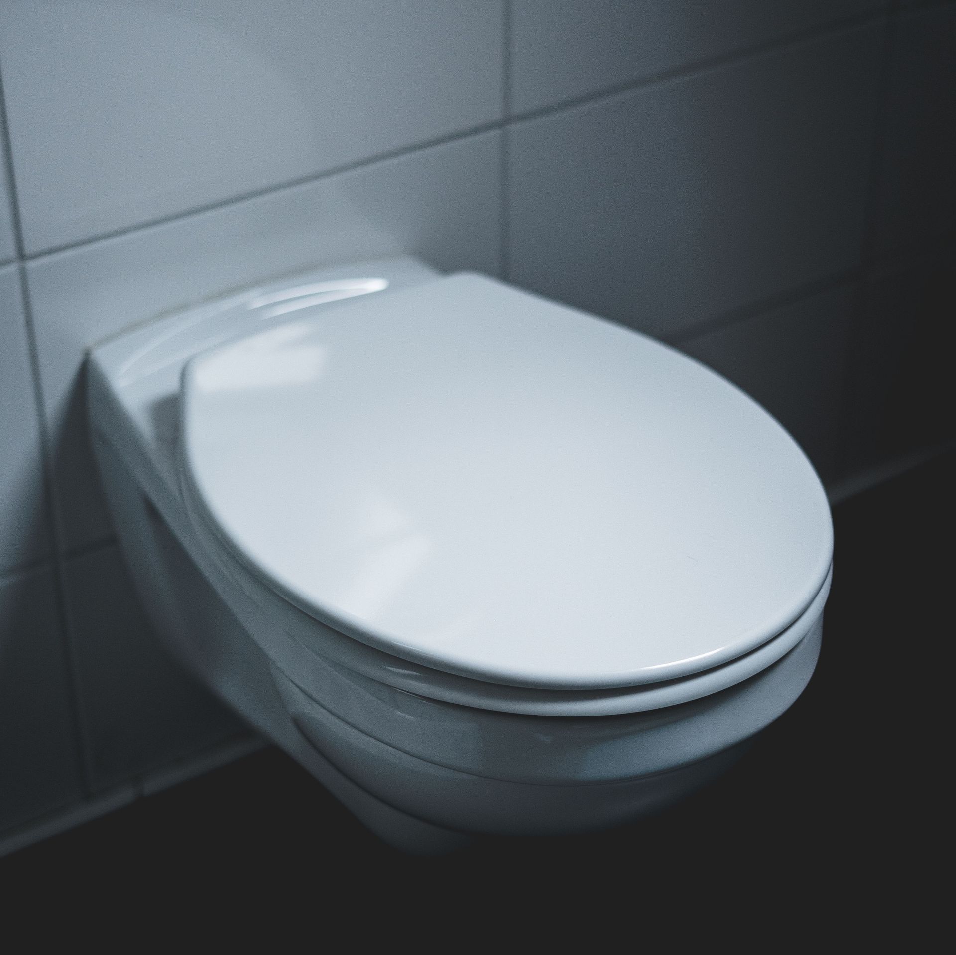 Closed white toilet against gray tiled wall