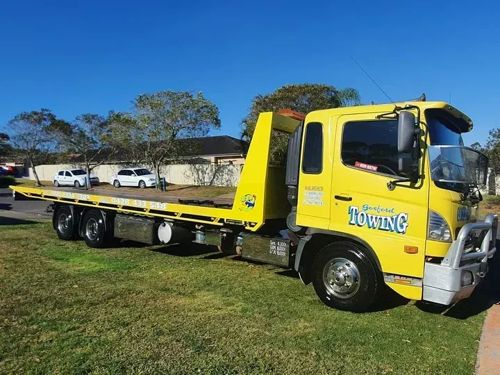 A yellow tow truck is parked in a grassy field.