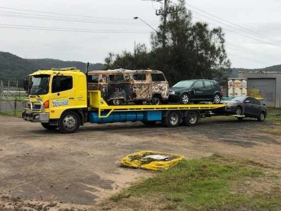 A yellow tow truck is carrying two cars and a van.