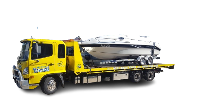 A yellow tow truck is carrying a boat on a trailer.