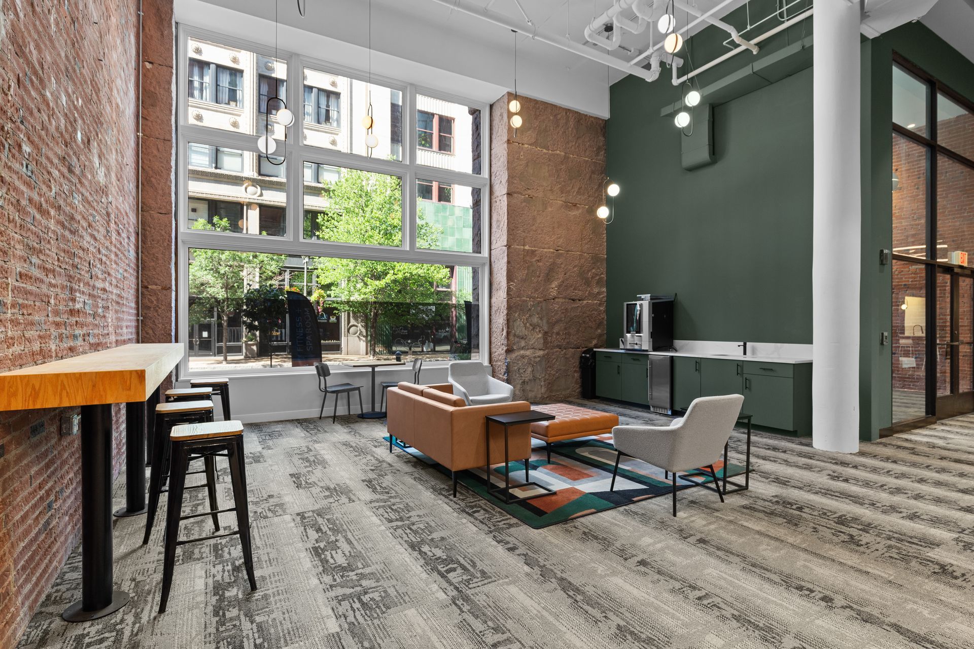 Modern loft lounge with large windows, green accent wall, sofas, chairs, and coffee tables on a patterned rug