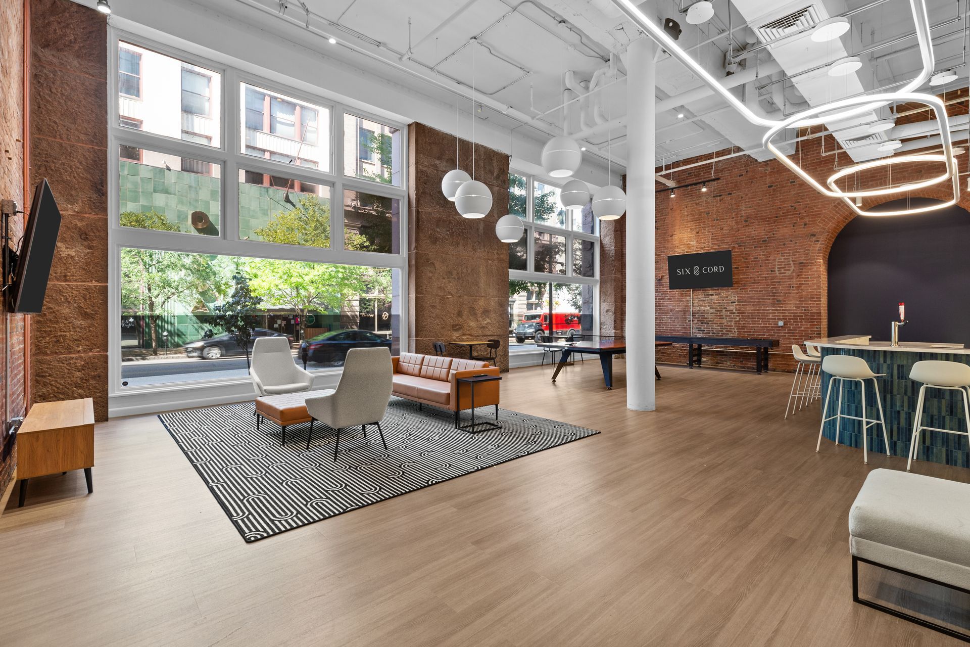Modern open office lounge with brick walls, large windows, and seating on a wood floor