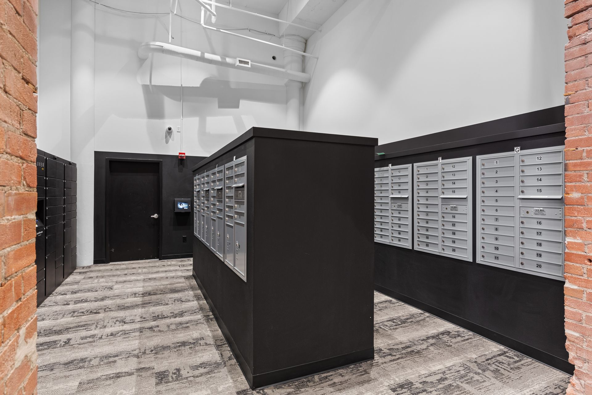 Modern lobby with black mailboxes, a dark door, and high white walls with exposed ducts