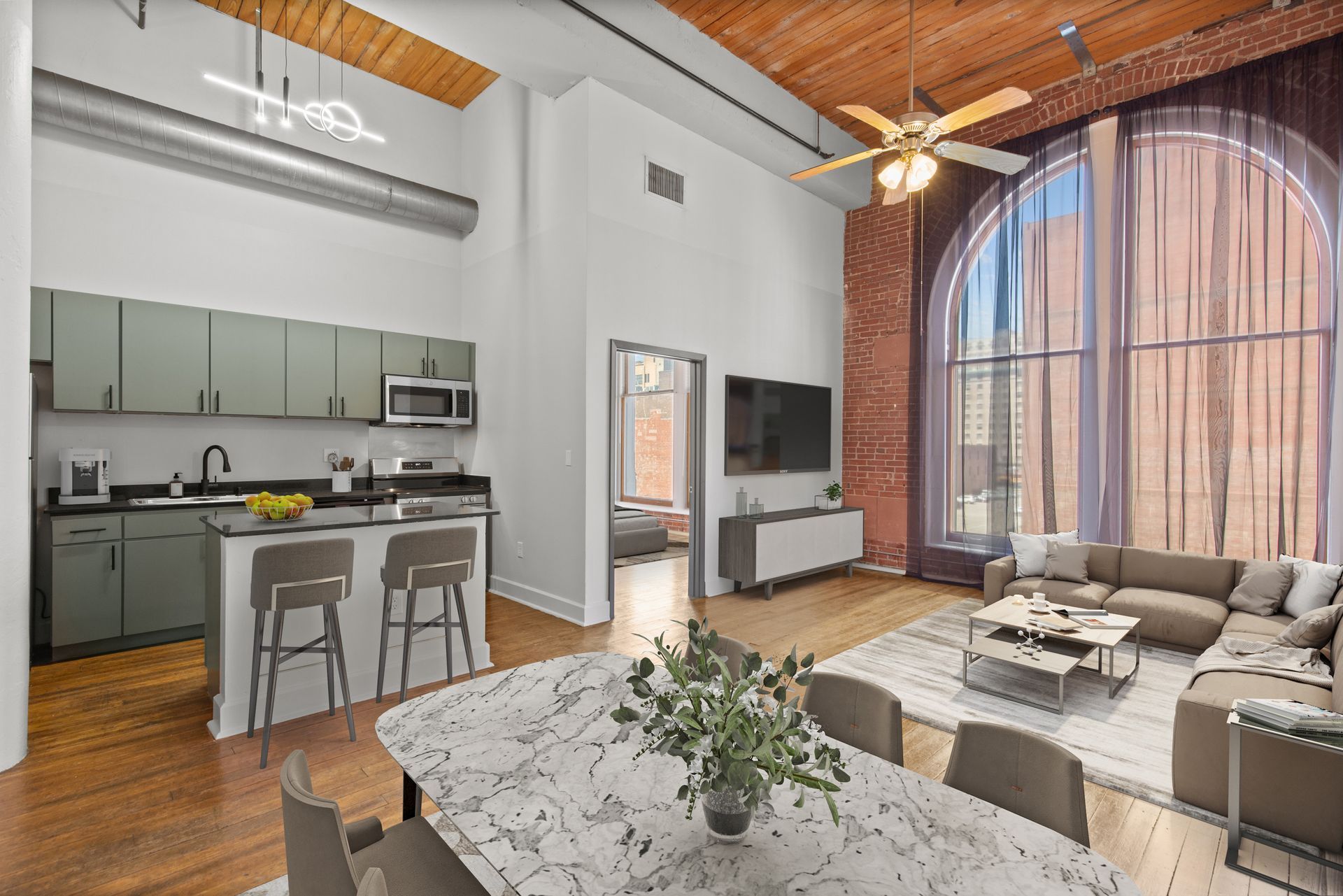 Modern loft living room with kitchen, beige sectional, marble table, and tall arched windows