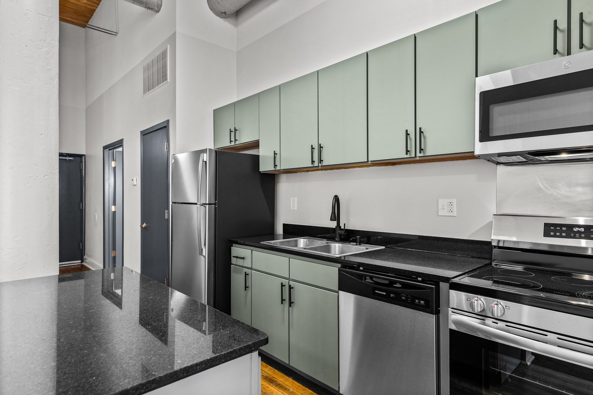 Modern kitchen with mint cabinets, black countertops, stainless steel appliances, and a black island table