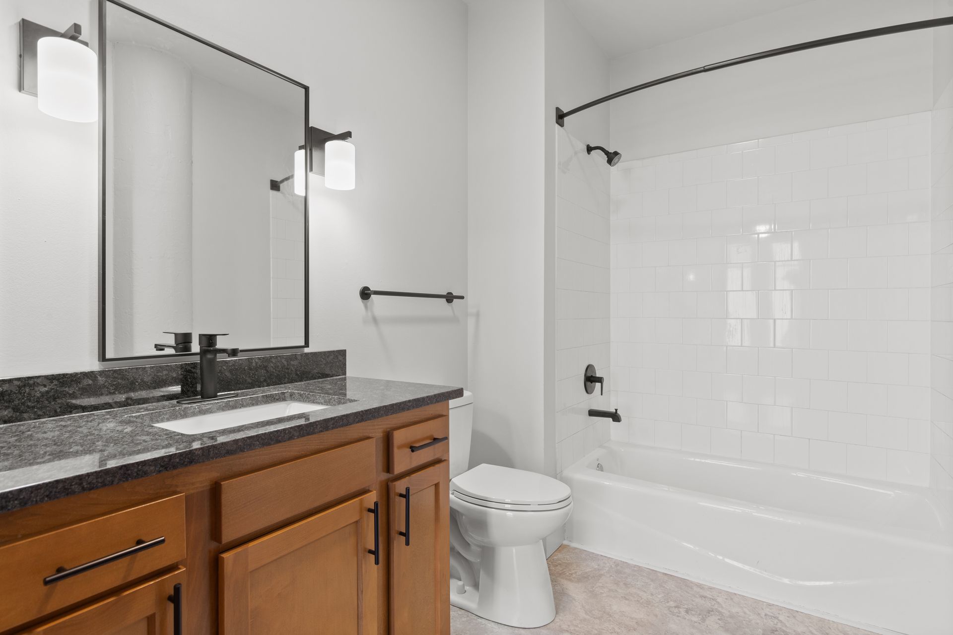Modern bathroom with granite vanity, large mirror, toilet, and white tiled bathtub/shower combo