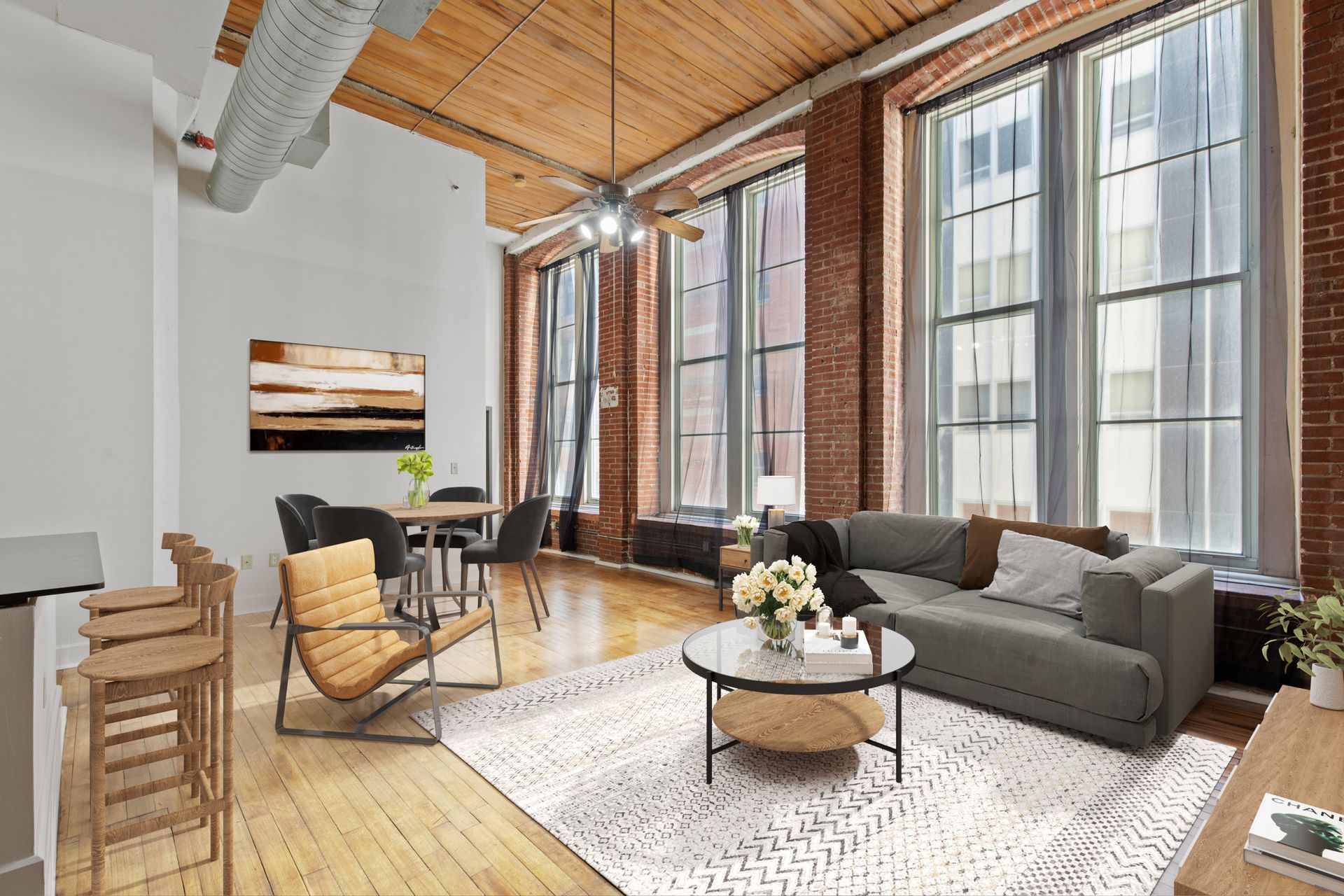 Modern loft living room with tall windows, exposed wood ceiling, gray sectional, and wicker chairs