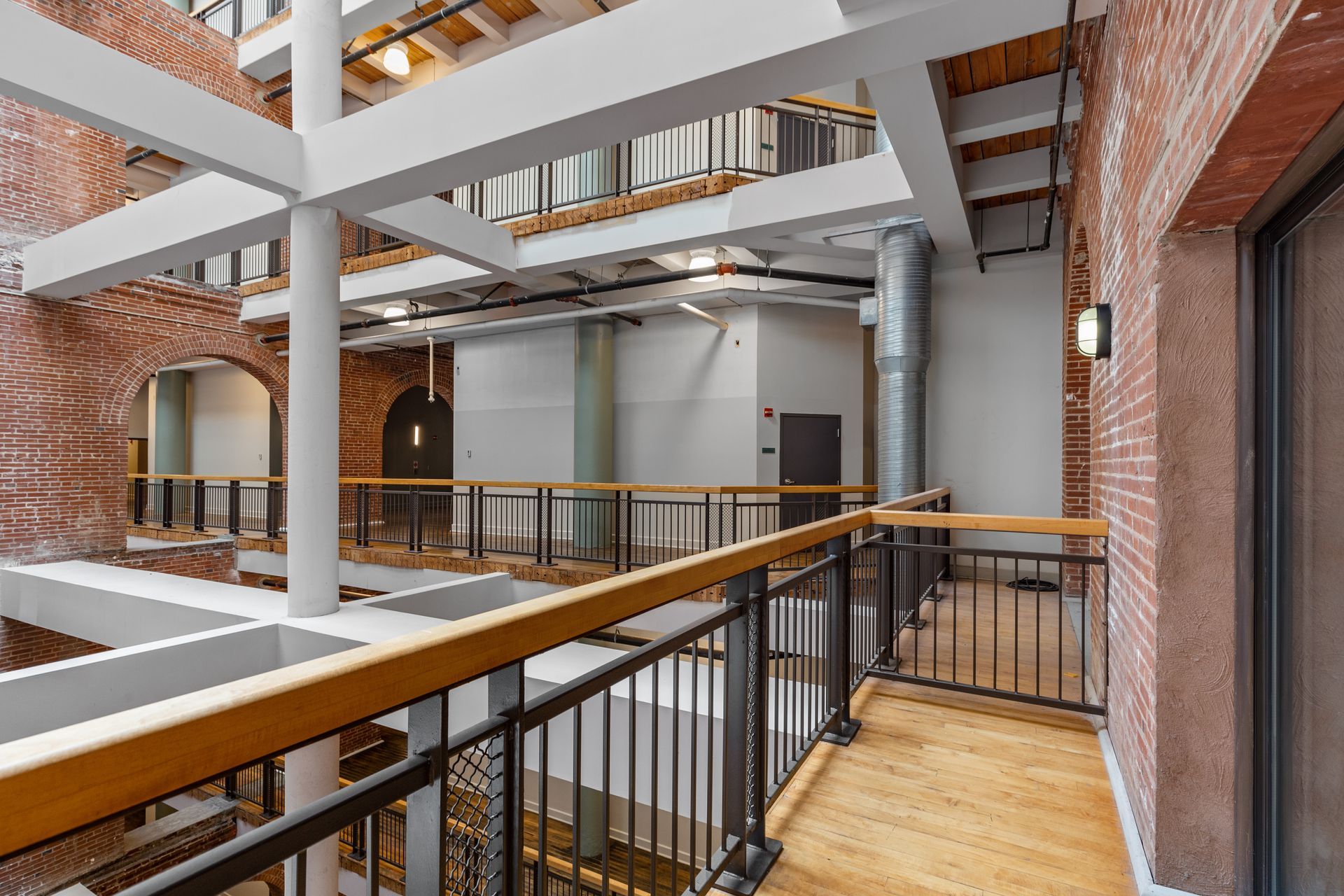 Modern atrium walkway with brick walls, exposed beams, and metal railings