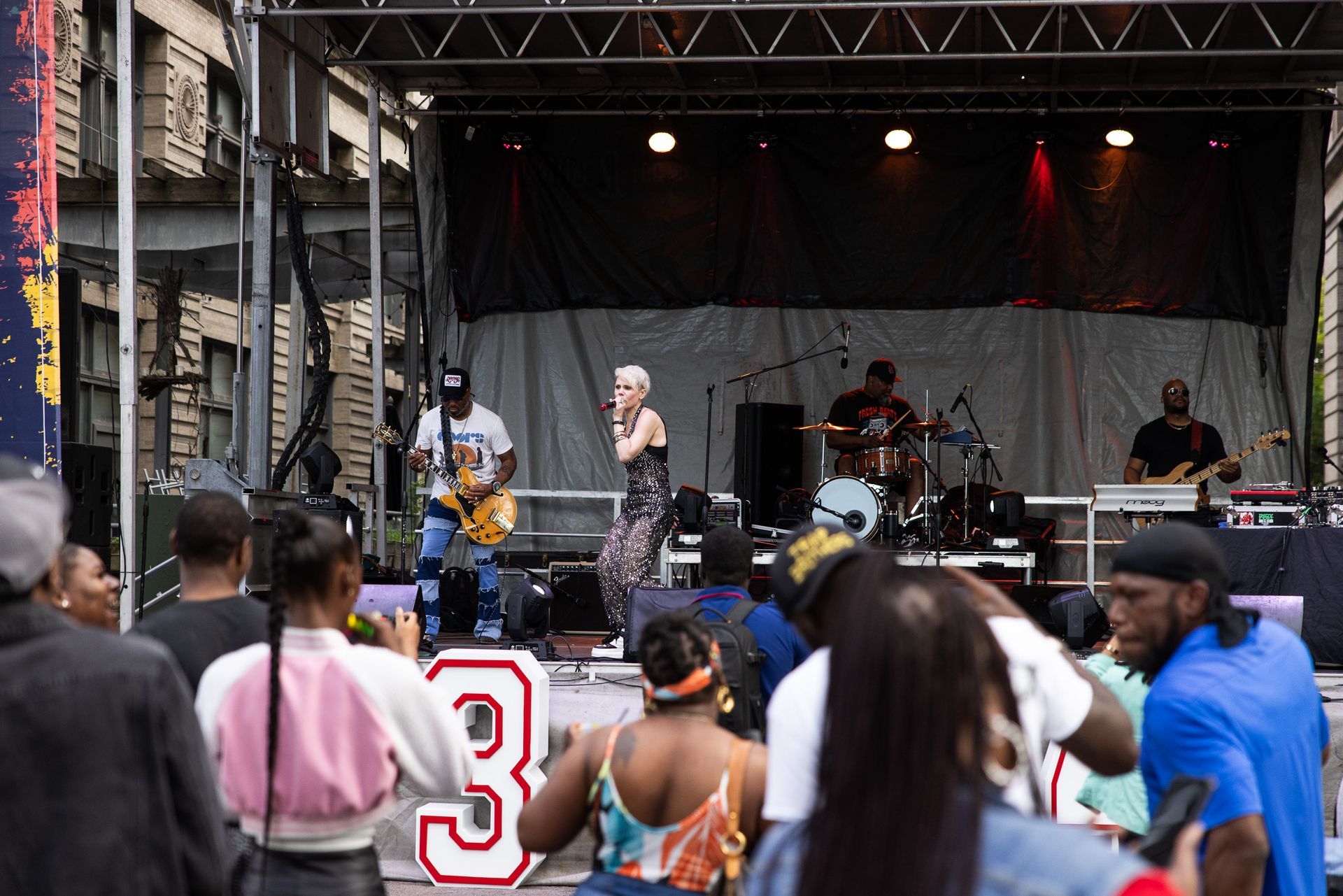 Outdoor stage performance with singer, band, and crowd watching in front