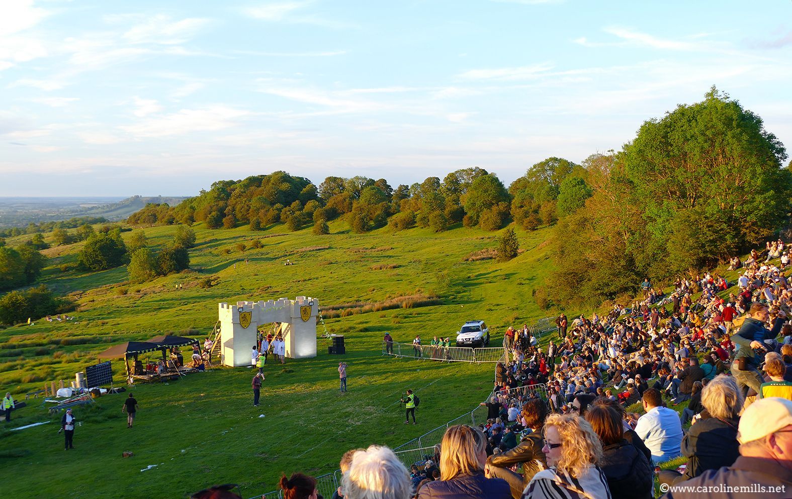 A large crowd of people are watching a performance in a field, the Cotswold Olympics