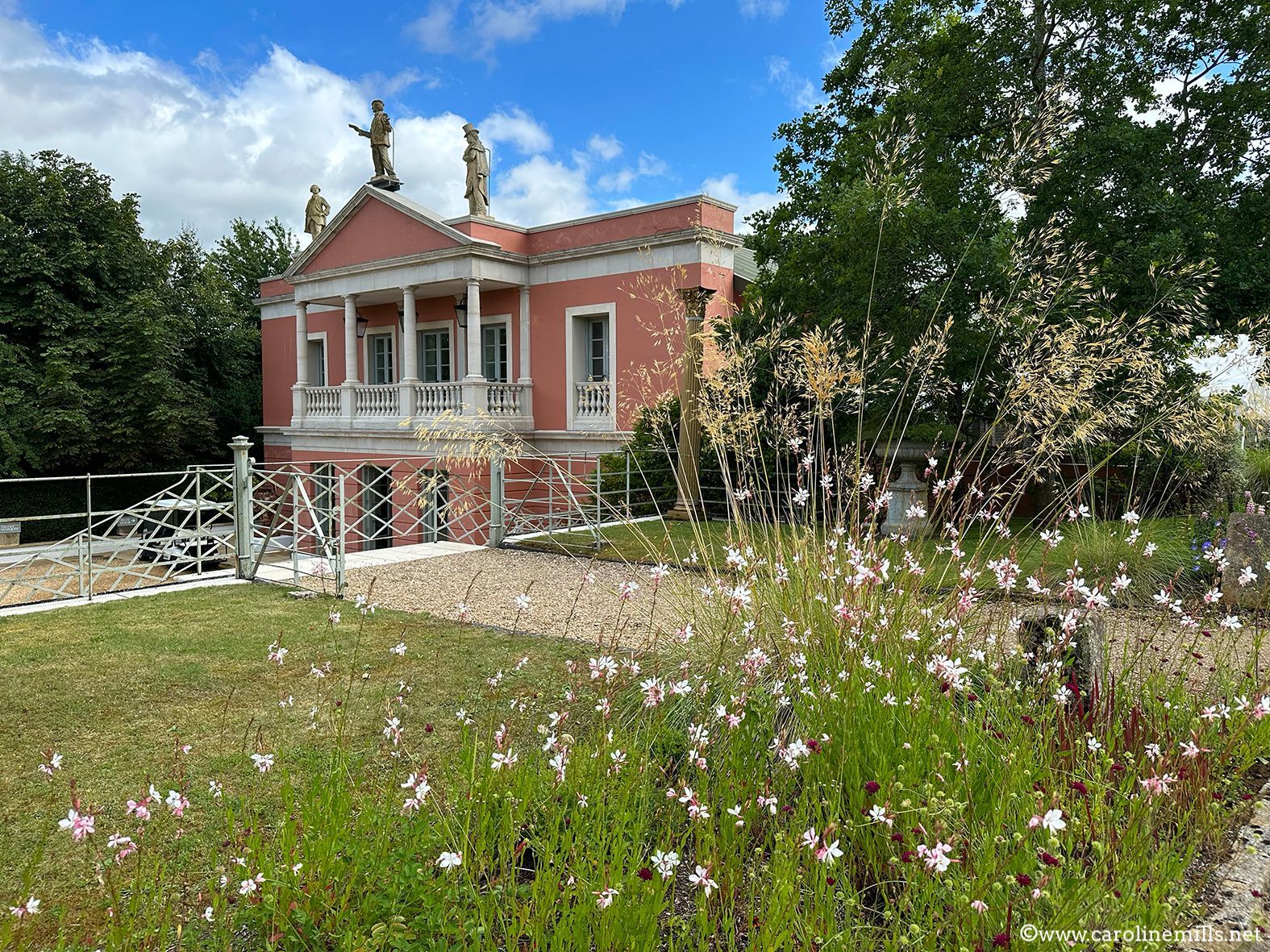 A large pink opera house is surrounded by flowers and trees.