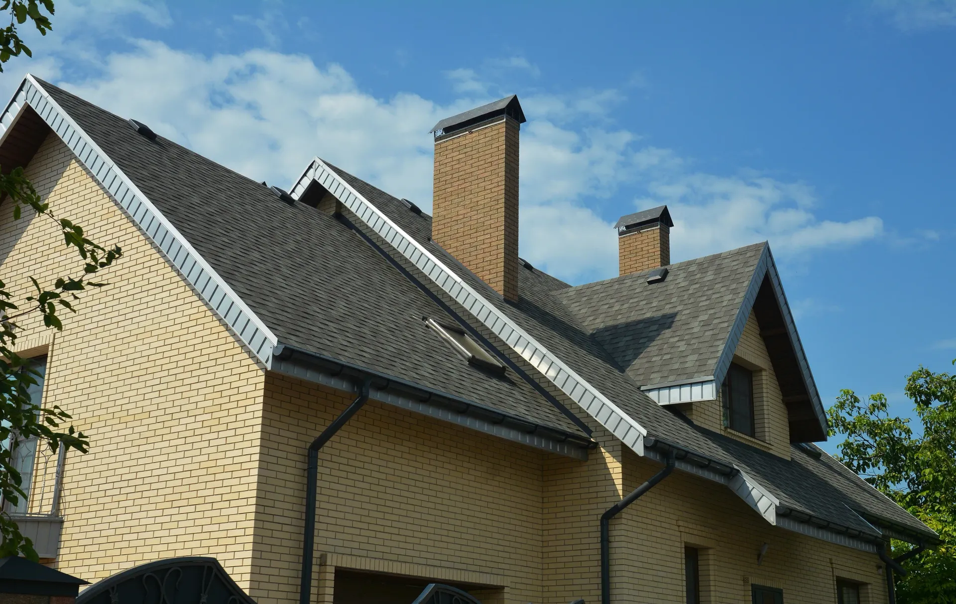 Brick house with dark gray roof and two chimneys under a blue sky