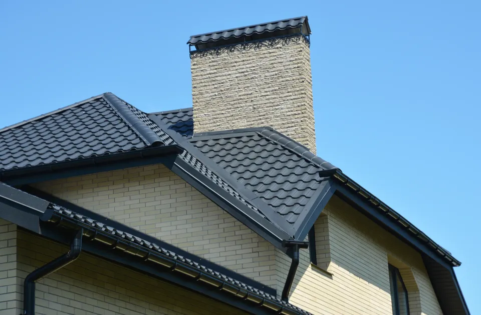 House roof with dark gray shingles and a brick chimney against a blue sky