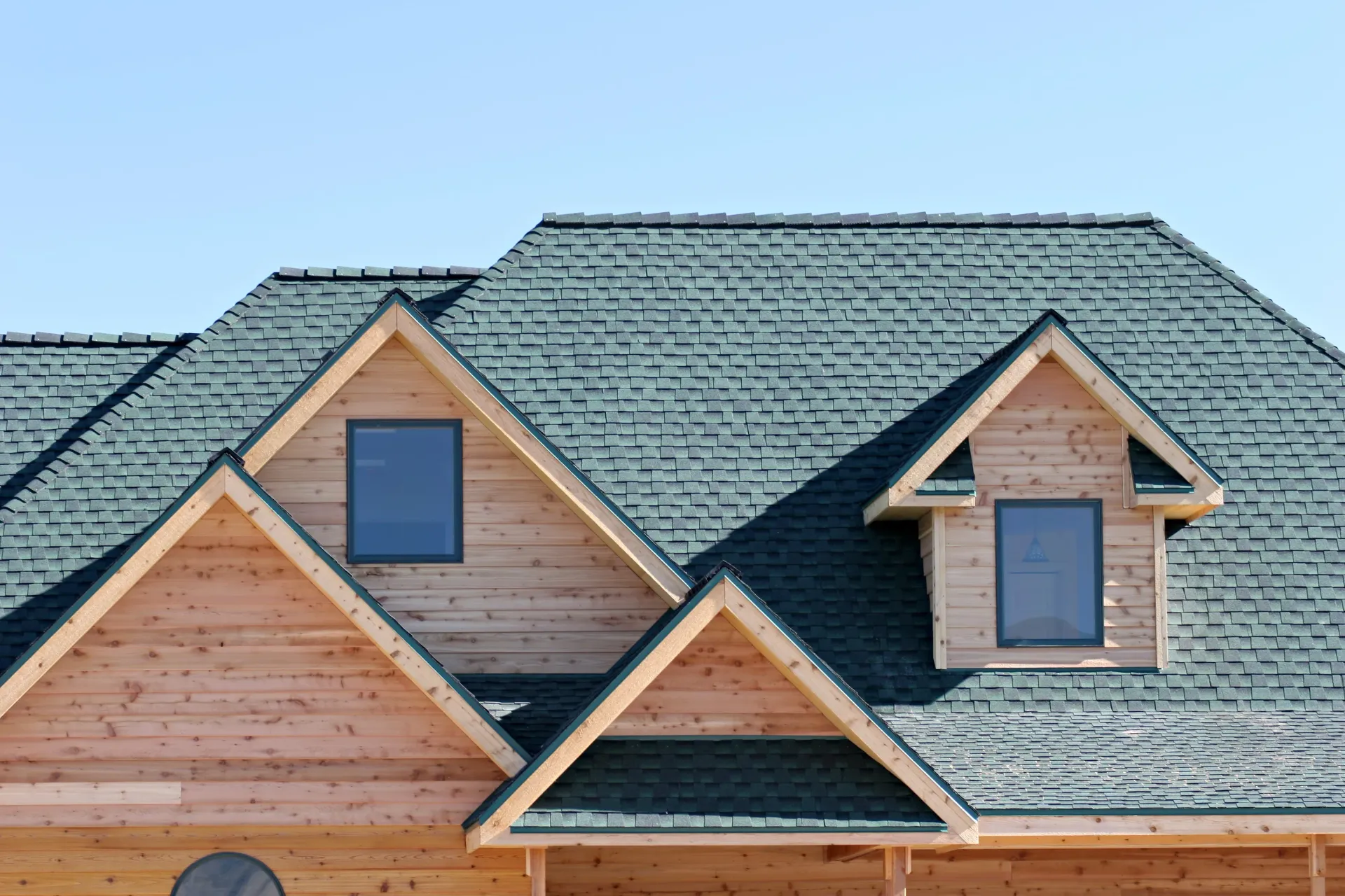 New house roof with green shingles and dormer windows against a blue sky
