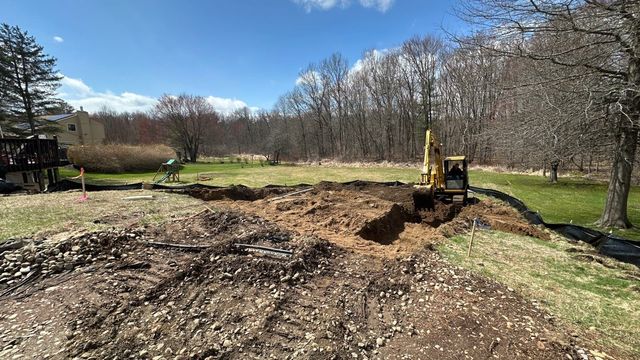 Yellow excavator digging a trench in a grassy field under a blue sky