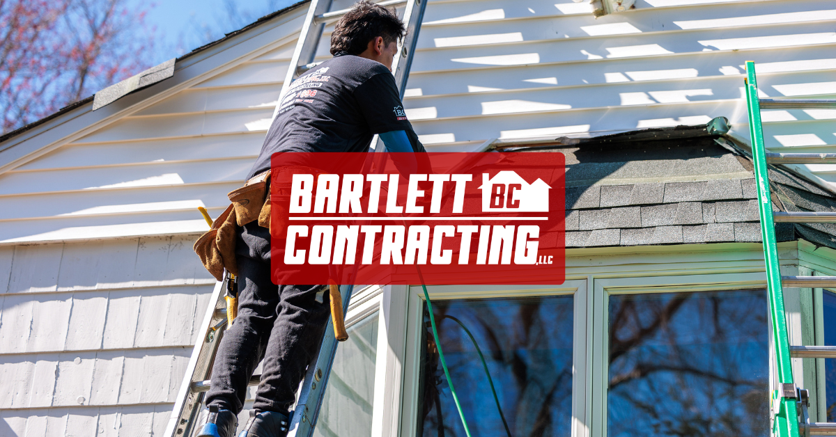 Contractor on ladder working on house exterior with Bartlett Contracting sign